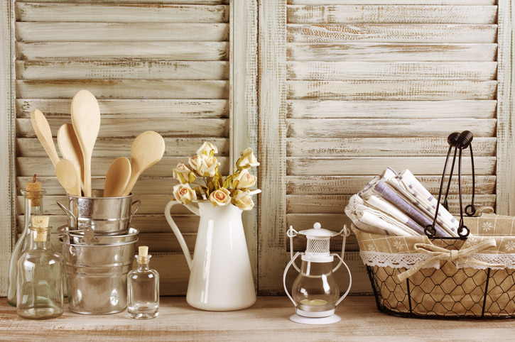Rustic elements on a wooden backgrounds. Vase with wooden utensils, basket with linen napkins and a white jug with dried flowers in it